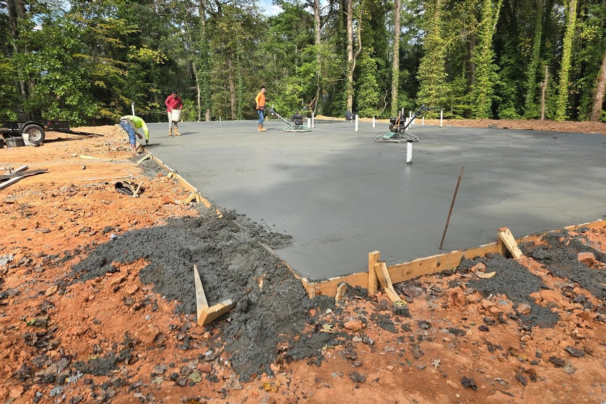 Crew screeding a fresh concrete slab pour on a wooded lot